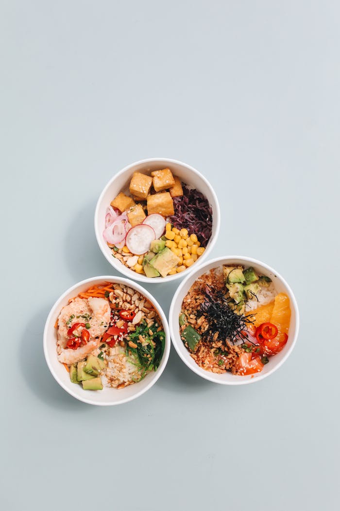 about-us Overhead view of three vibrant poke bowls with fresh ingredients on a pastel background.
