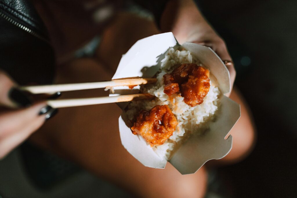 pexels photo 6646264 6646264 Fried shrimp with rice in a takeout box, held with chopsticks, exuding Asian culinary appeal.